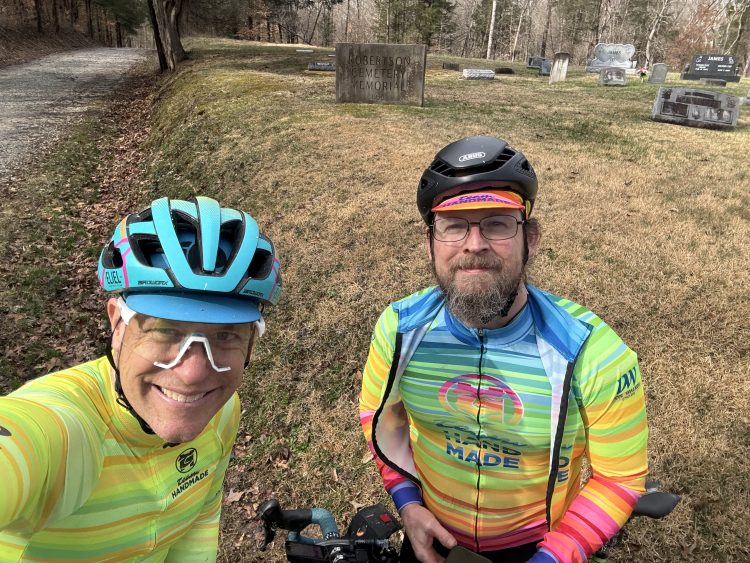 Chris Carville and Travis posing for a selfie near the trail with an old cemetary in the background